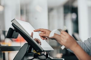A person holding a receipt and putting something on the touch screen till screen